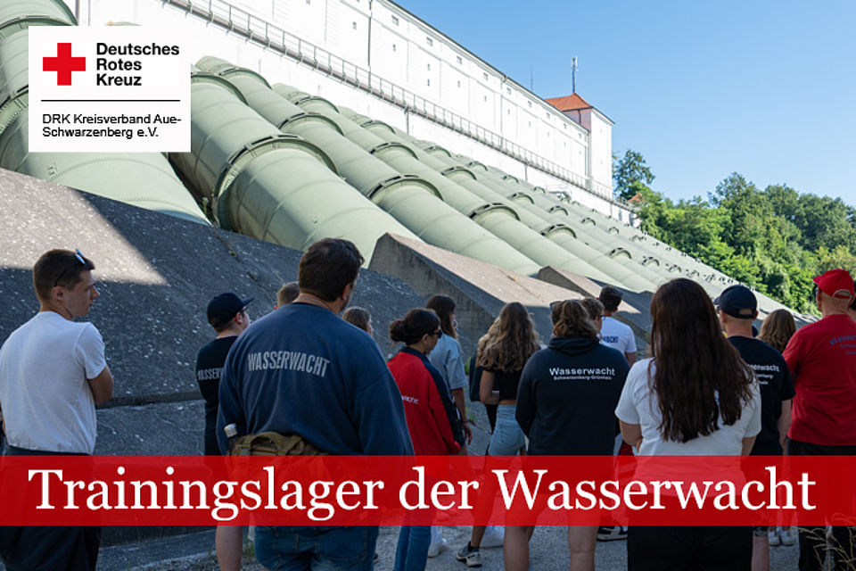 Personengruppe mit Wasserwacht-Kleidung vor Rohrsystem eines Wasserkraftwerkes